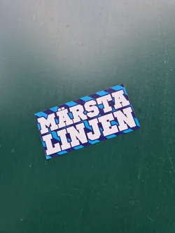 A blue and white sticker with the text "Märsta Linjen" on it. The text is in a bold, sans-serif font. The sticker has a diagonal stripe pattern.