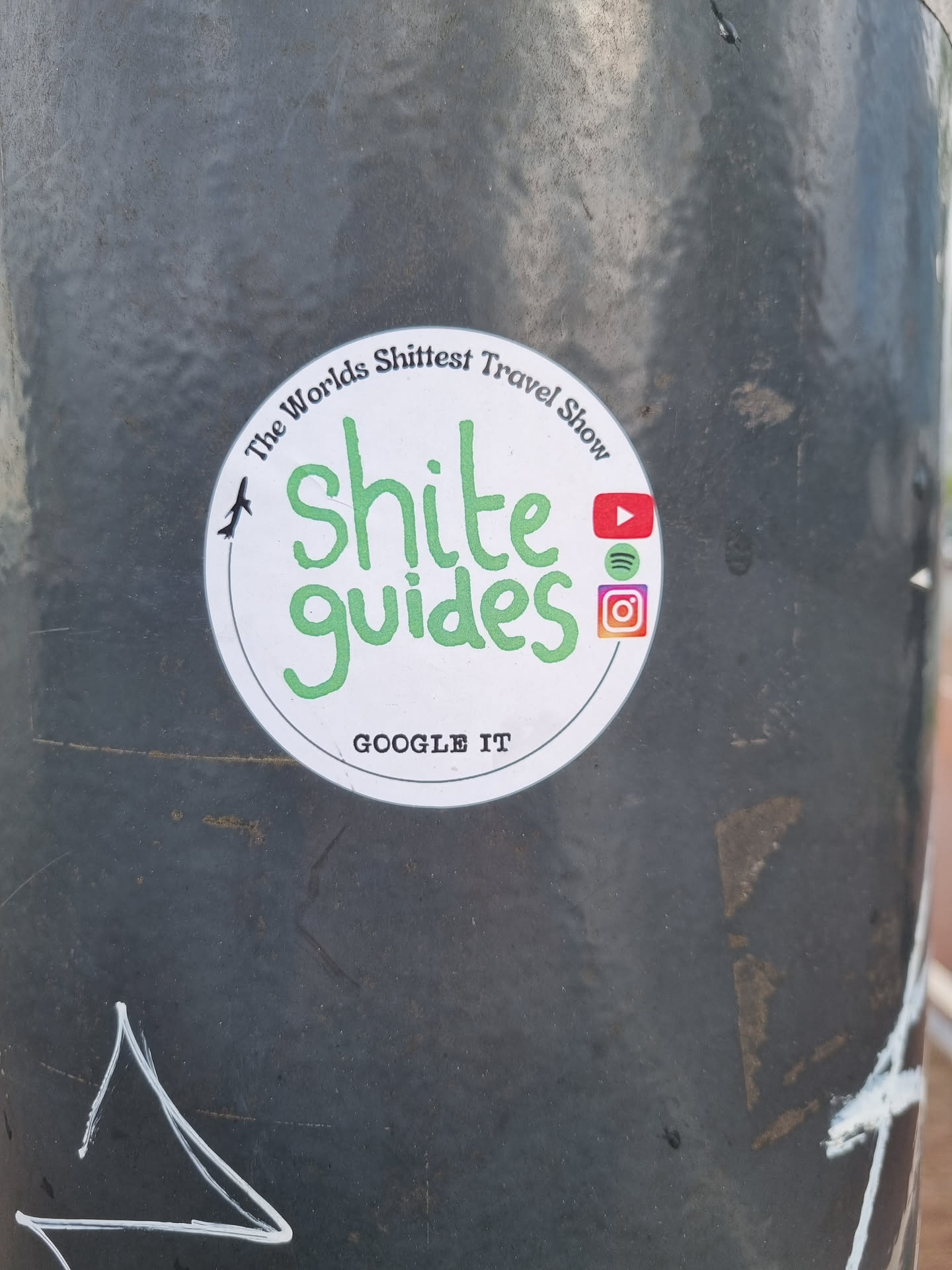 Round sticker with green text on a white background.  It says "Shîte guides" in a stylized font.  At the top it says "The World's Shittest Travel Show" in a smaller font. At the bottom it says "Google it". There are also social media icons for YouTube, Spotify and Instagram.