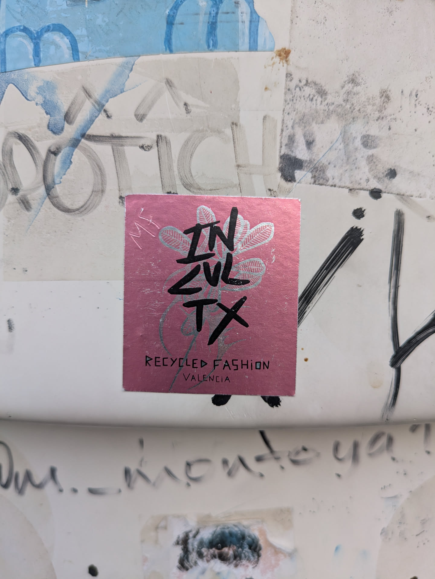 A pink square sticker that reads "INZUL TX Recycled Fashion Valencia". The design includes black lettering and a decorative silver plant motif.