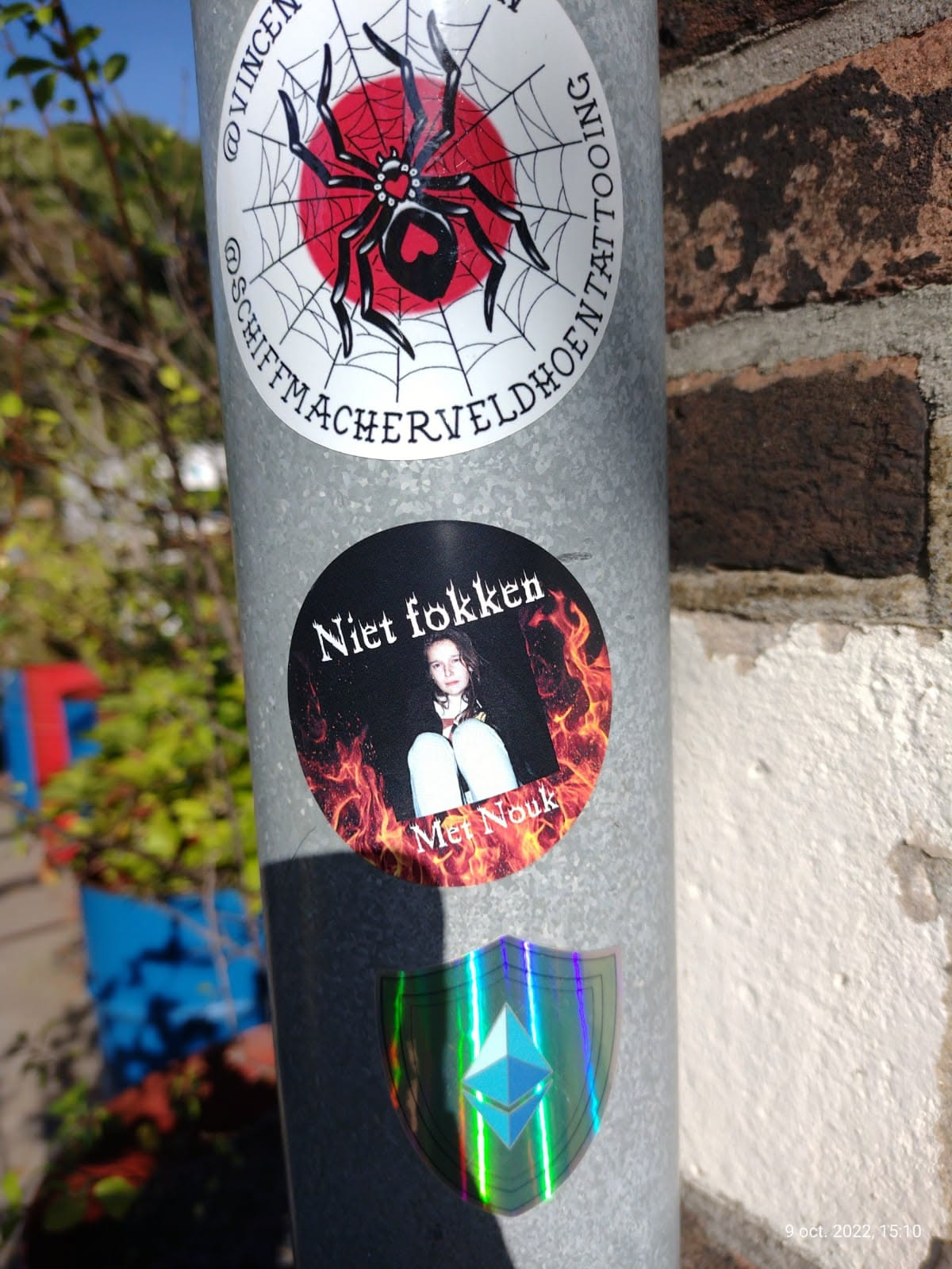 A round sticker with a picture of a girl sitting on the floor in flames. The text on the sticker says "Niet fokken" which is Dutch for "Don't fuck" and "Met Nouk" which might be a name.