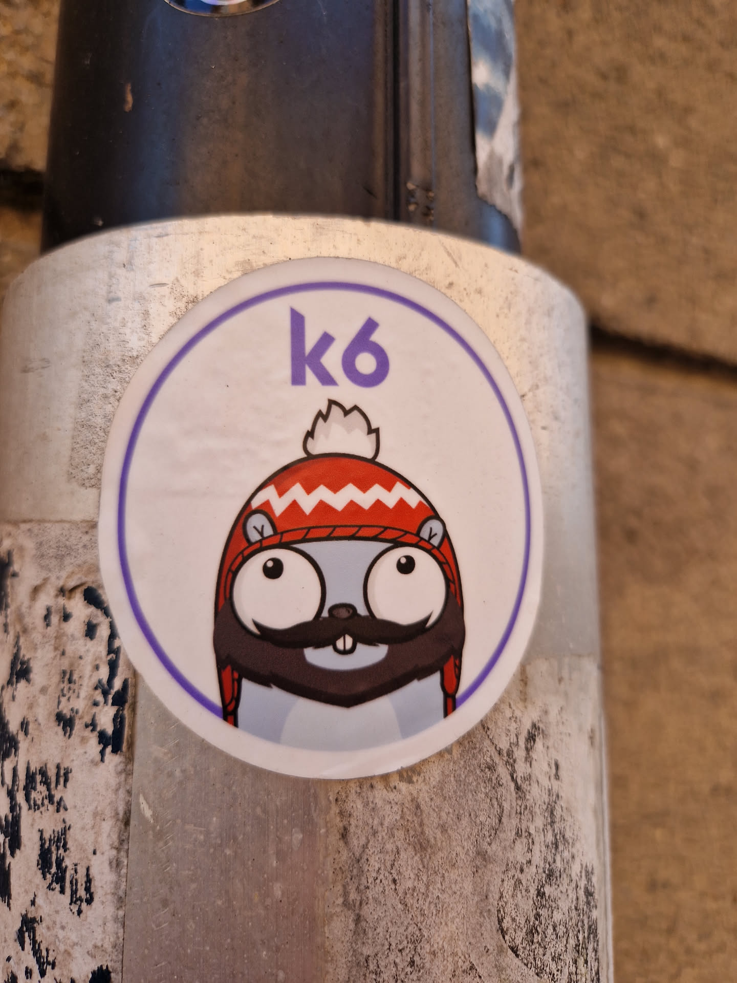 Round sticker featuring the k6 mascot, a gopher wearing a red and white winter hat with a pompom. The mascot has large eyes and a mustache. The text "k6" is displayed in purple at the top of the sticker.