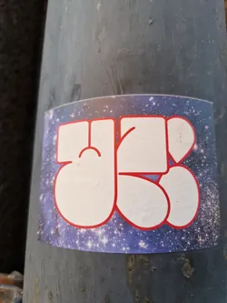 A sticker featuring a stylized design with white characters outlined in red against a deep blue cosmic background of twinkling stars. The characters appear abstract or possibly represent letters or symbols.