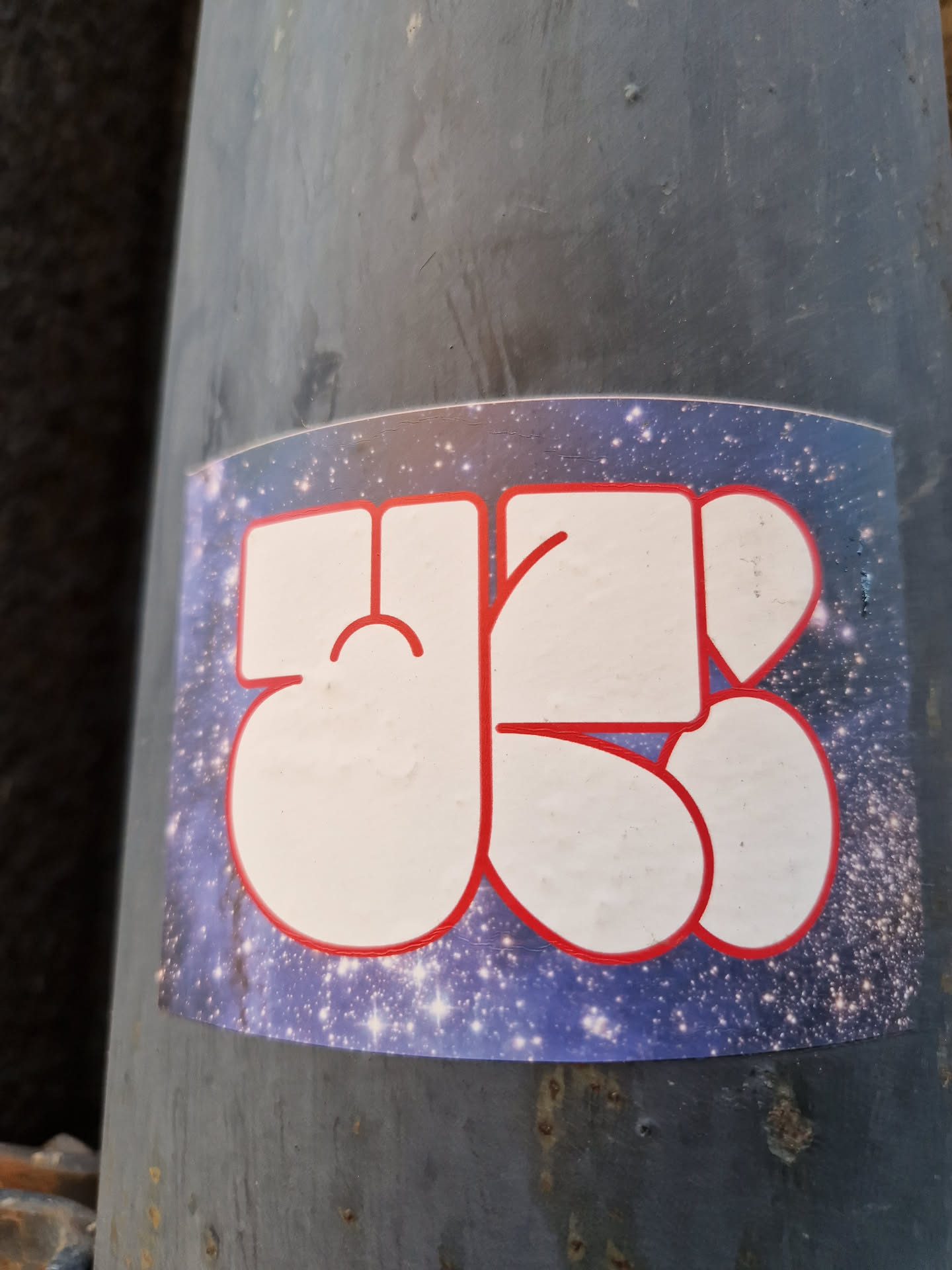 A sticker featuring a stylized design with white characters outlined in red against a deep blue cosmic background of twinkling stars. The characters appear abstract or possibly represent letters or symbols.