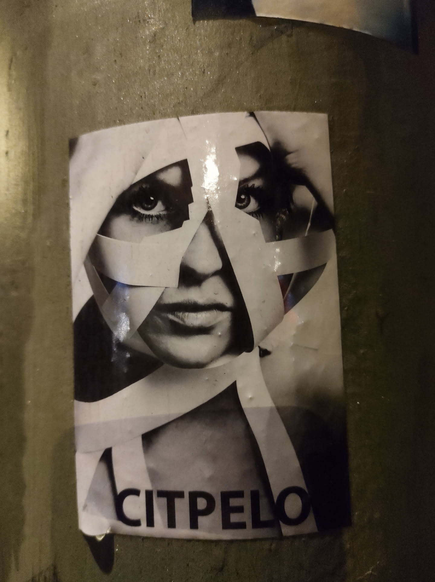 Black and white sticker featuring a woman's face partially obscured by pieces of tape. The word CITPELO is visible at the bottom. 
