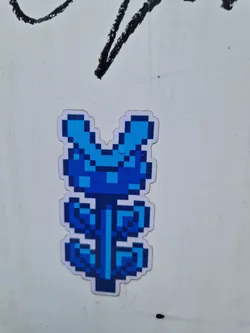 A blue pixel art flower sticker on a white background. The flower is simple but cute. It looks like it's been stuck to a wall or other surface.
