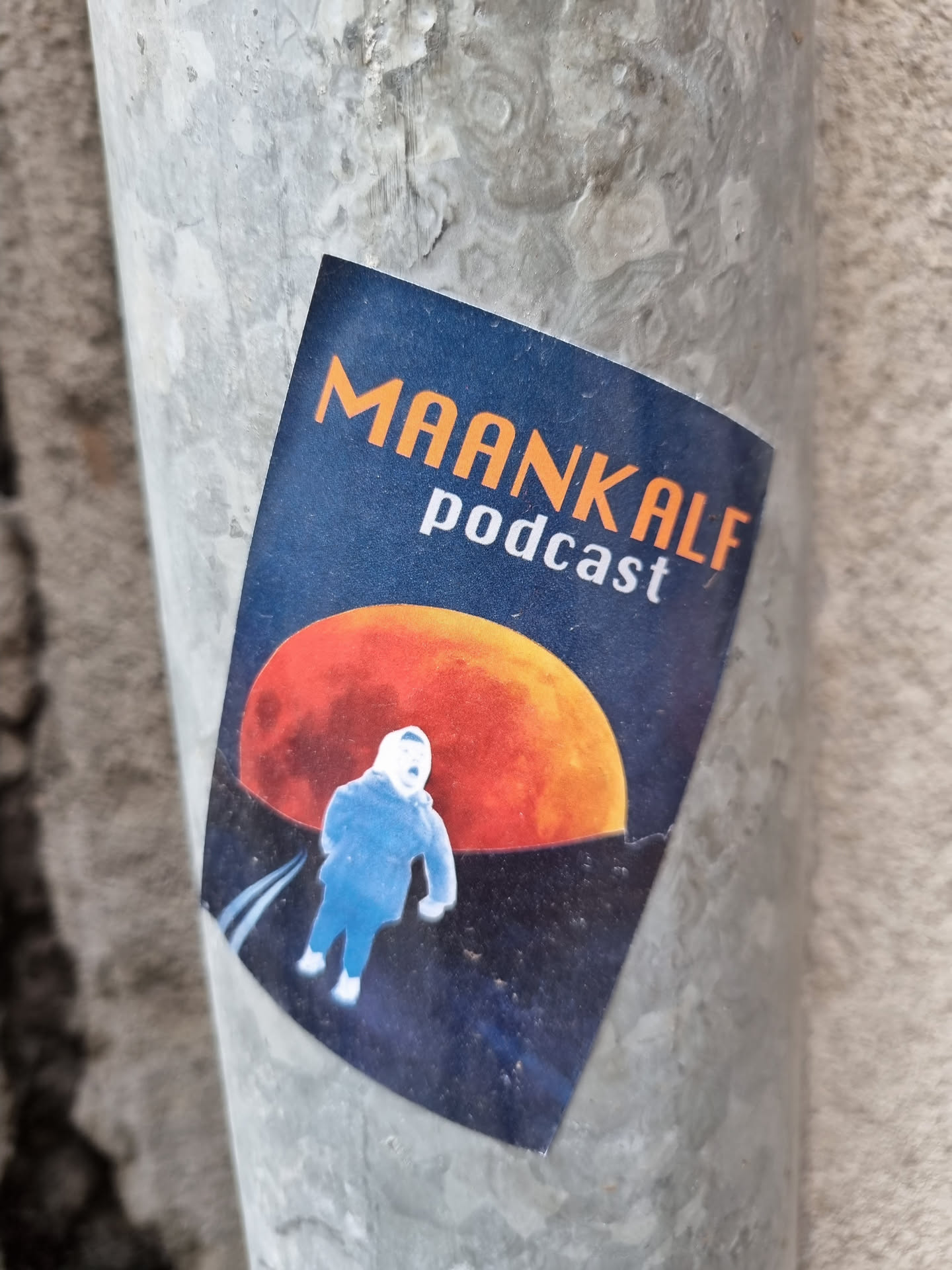 A sticker featuring the Maankalf podcast logo. The design includes an illustration of a child walking on a road towards a large orange moon. The color scheme is dark blue and orange.