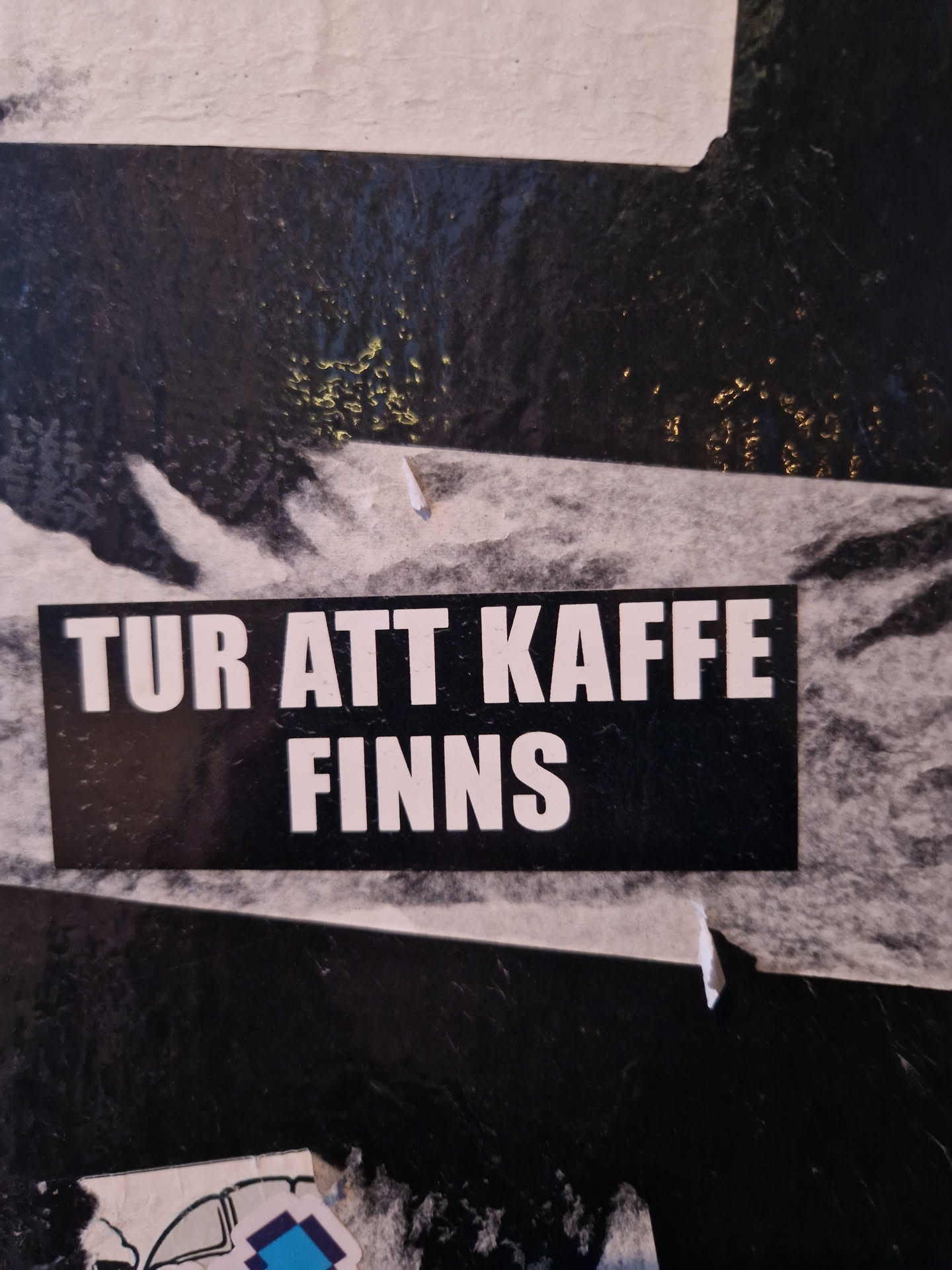 A black and white sticker with the text "TUR ATT KAFFE FINNS" (Swedish for "Time for coffee exists") on it. The sticker is attached to a dark surface. 