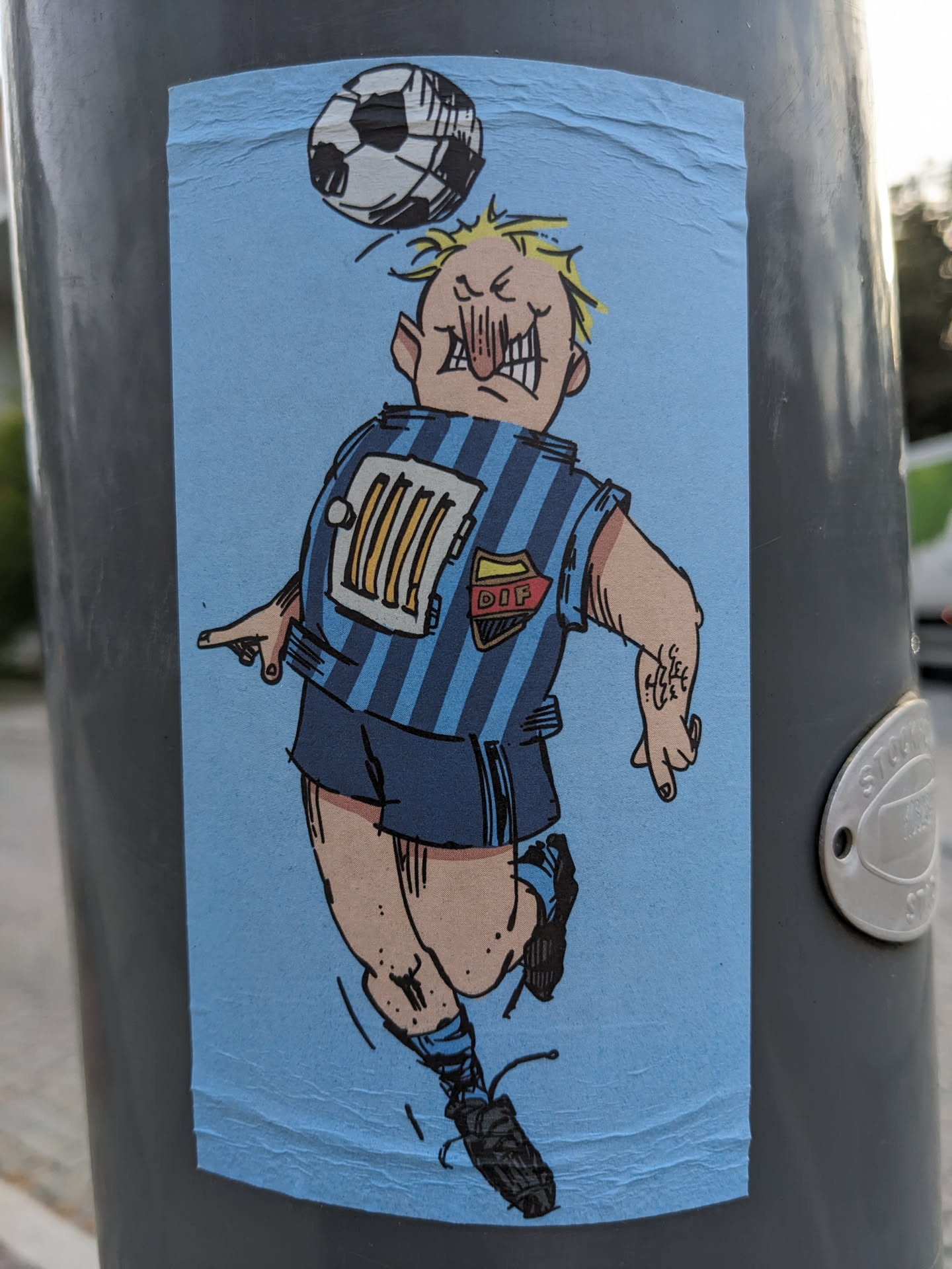 The sticker features a hand-drawn illustration of a cartoonish soccer player with exaggerated features. He's depicted in mid-air, heading a soccer ball. The style is reminiscent of comic books or graphic novels. The player's jersey is blue with a unique design featuring a radiator graphic and the acronym "DIP." The overall color palette is simple, using mainly blues and light tones.