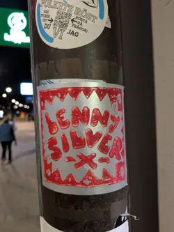 This sticker features the text 'LENNY SILVER' in a stylized, somewhat dripping red font on a metallic silver background. The sticker's border is decorated with a sawtooth pattern, also in red. The overall look is reminiscent of hand-drawn or stencil art.