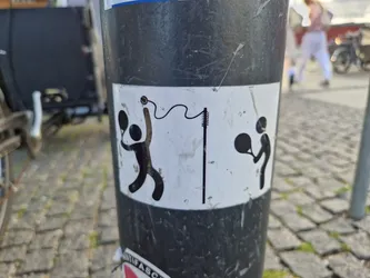 A sticker featuring a minimalist design of two figures playing tennis. One is serving, the other receiving. A tennis net is also depicted. The style is simple and playful.