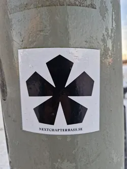 A white square sticker featuring a black, stylized flower or starburst graphic.  Text at the bottom reads 'NEXTCHAPTERBASS.SE'.