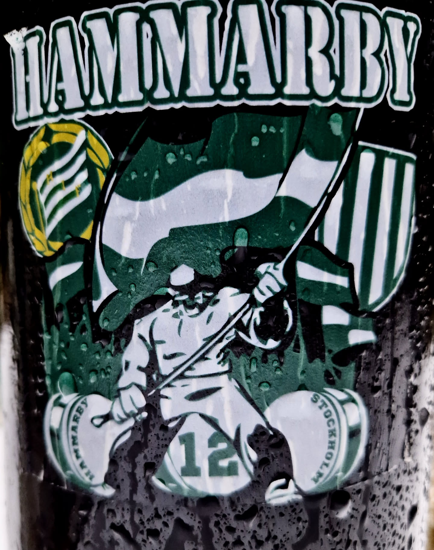 A sticker featuring the Hammarby Football Club logo. It includes the club's name, a figure with a pole, and the number 12. The sticker is wet and has water droplets on it.