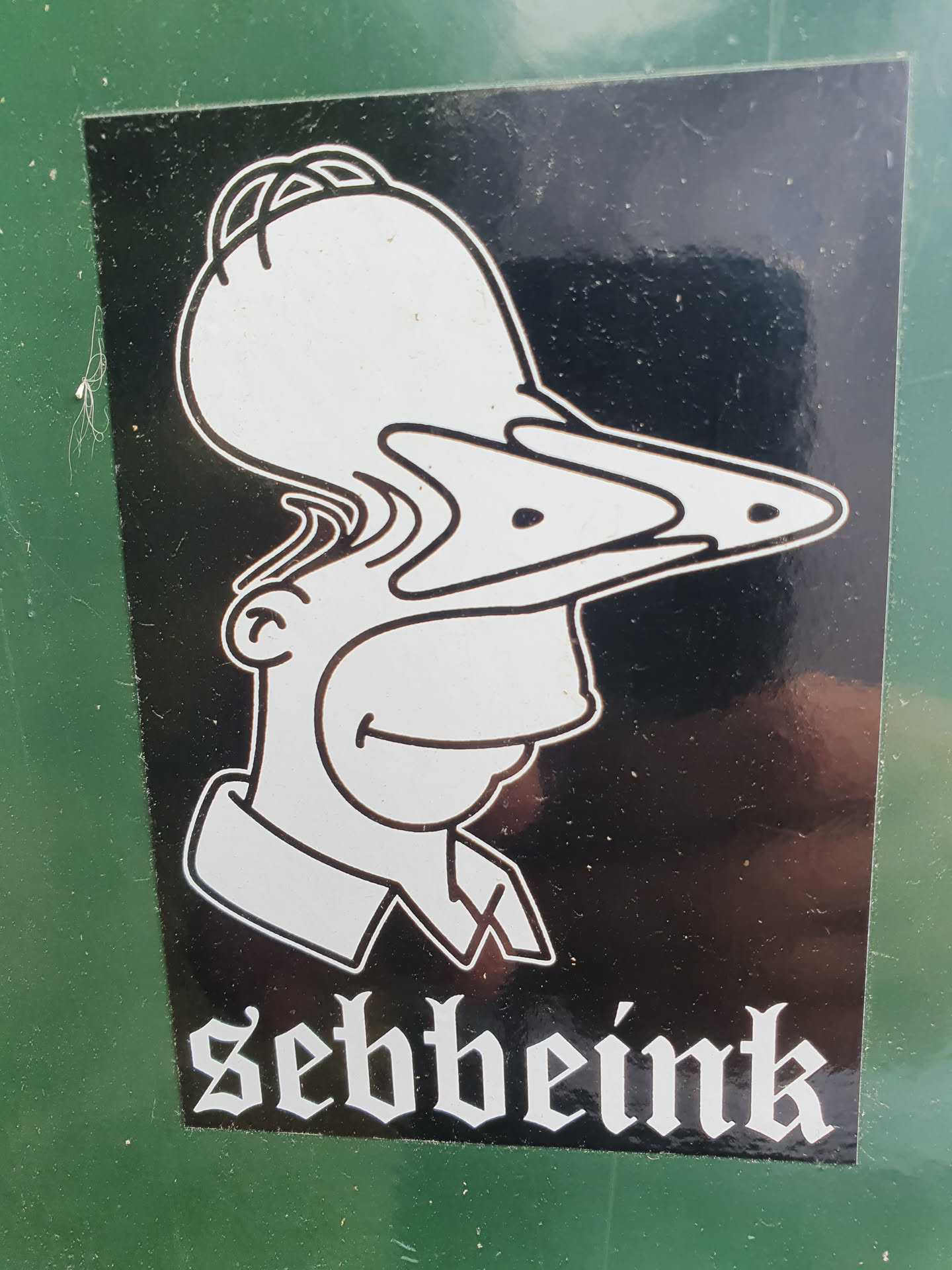 Black and white sticker featuring a distorted illustration of Homer Simpson with three noses.  The artist's name, "Sebbeink", is printed in a gothic-style font below the image.
