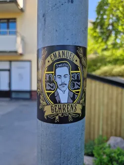 Black and gold sticker featuring an illustration of Emanuel Behrens. The design includes decorative flourishes and a banner with the name 'Behrens'.