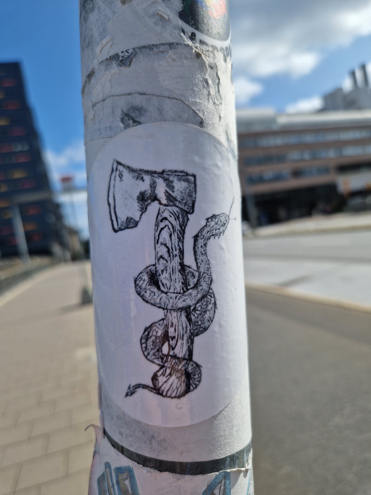 Black and white illustration of an axe with a snake wrapped around the handle. The sticker is slightly worn but the image is still visible.