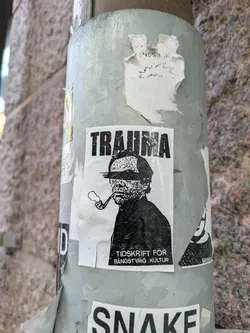 Black and white sticker featuring a man smoking a pipe, with the word "TRAUMA" written above him. Below is text that reads "TIDSKRIFT FÖR BÅNGSTYRIg KULTUR".
