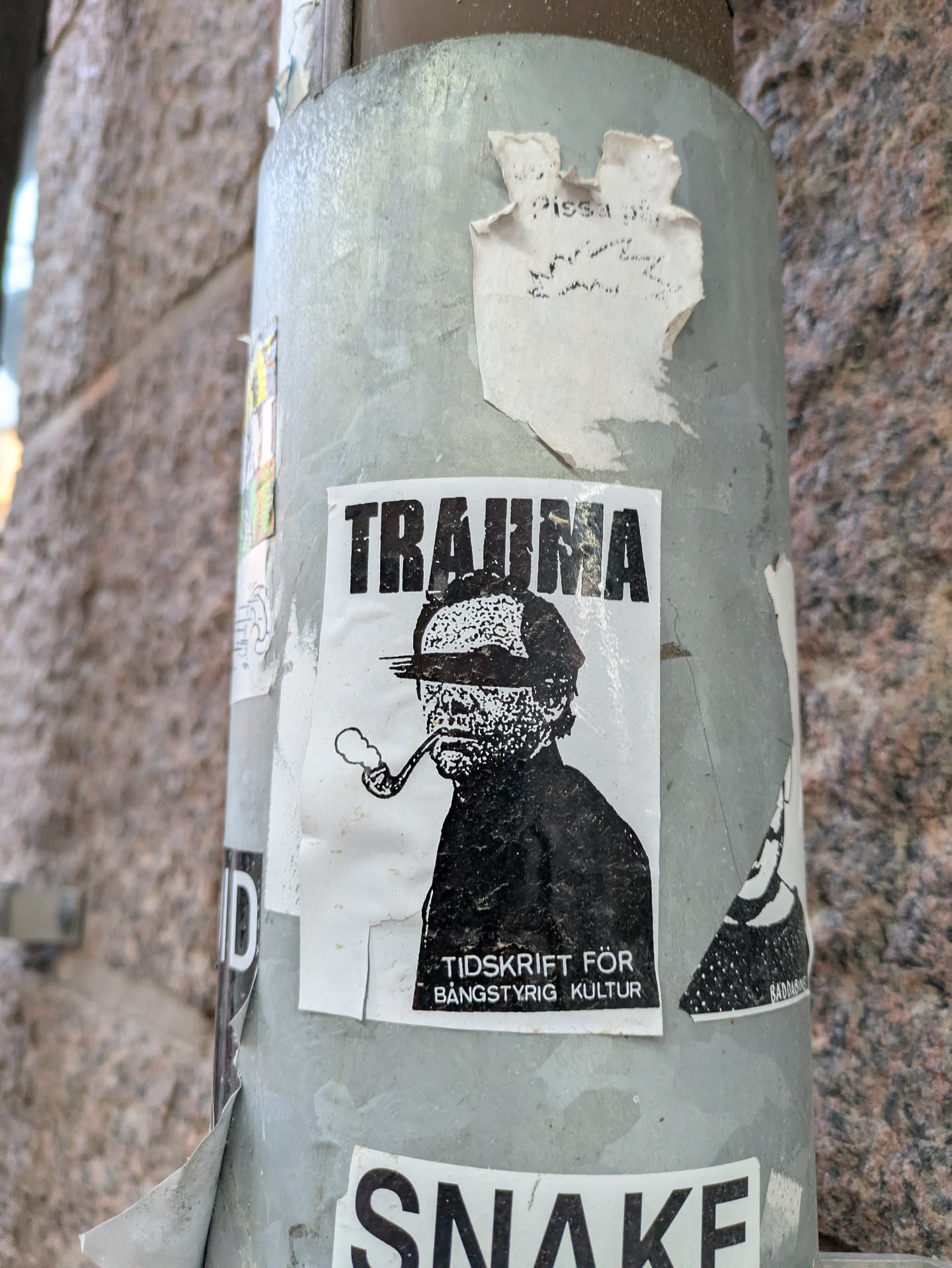 Black and white sticker featuring a man smoking a pipe, with the word "TRAUMA" written above him. Below is text that reads "TIDSKRIFT FÖR BÅNGSTYRIg KULTUR".