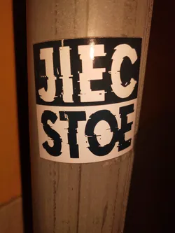 A black and white sticker with the text "JIEC STOE" written in a bold, distorted font. The sticker is affixed to a metallic pole.