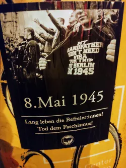 A sticker commemorating the end of World War II in Europe, featuring a photo of soldiers and the text "My grandfather didn't need a visa for a trip to Berlin in 1945". The sticker also includes the date 8. Mai 1945 and the slogans "Long live the liberators!" and "Death to fascism!"