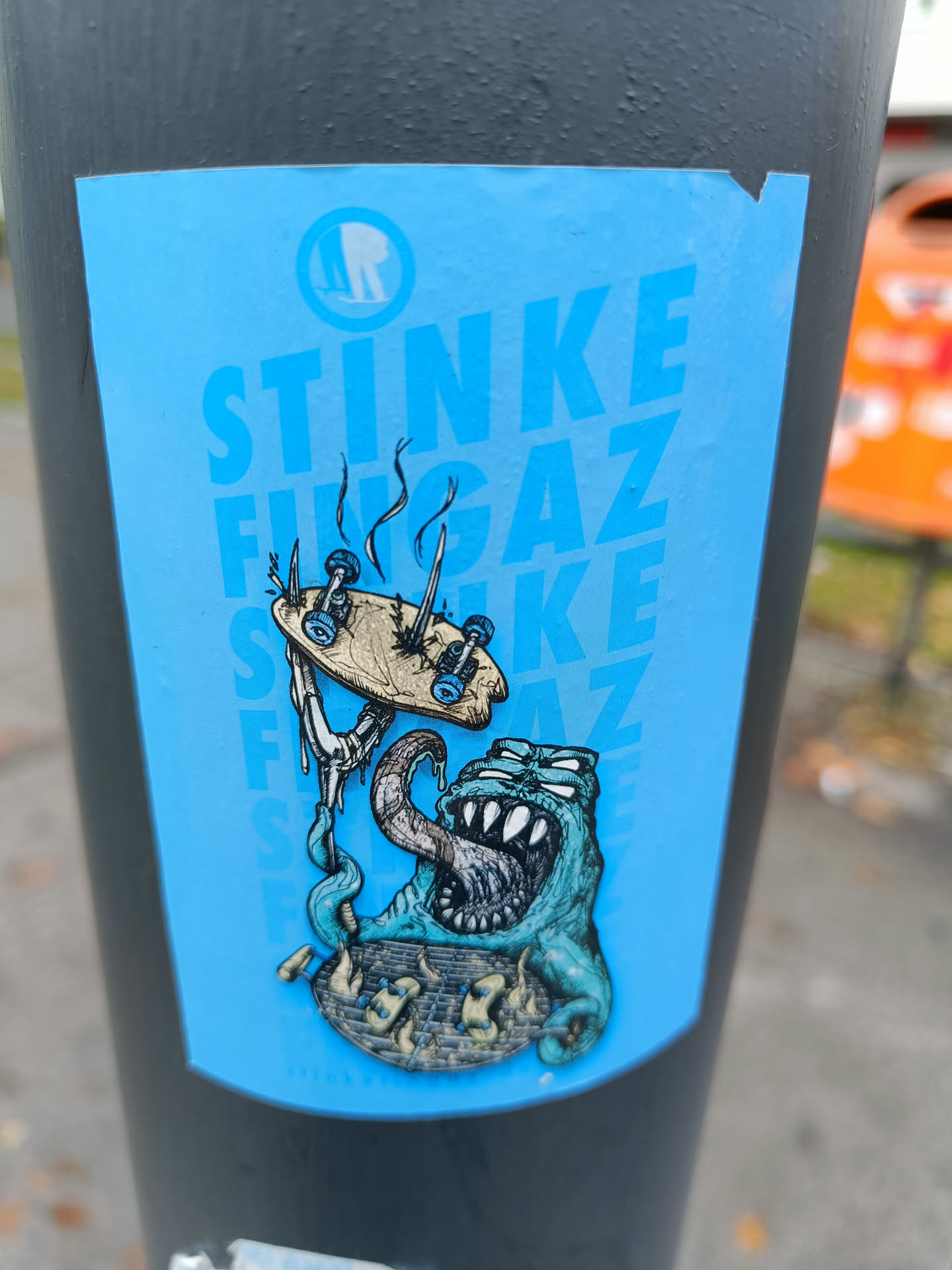 A sticker featuring a cartoon monster devouring a broken skateboard on a light blue background. The word "STINKE FUNGAZ" is repeated vertically on the sticker. There is a logo in a circle at the top left corner.