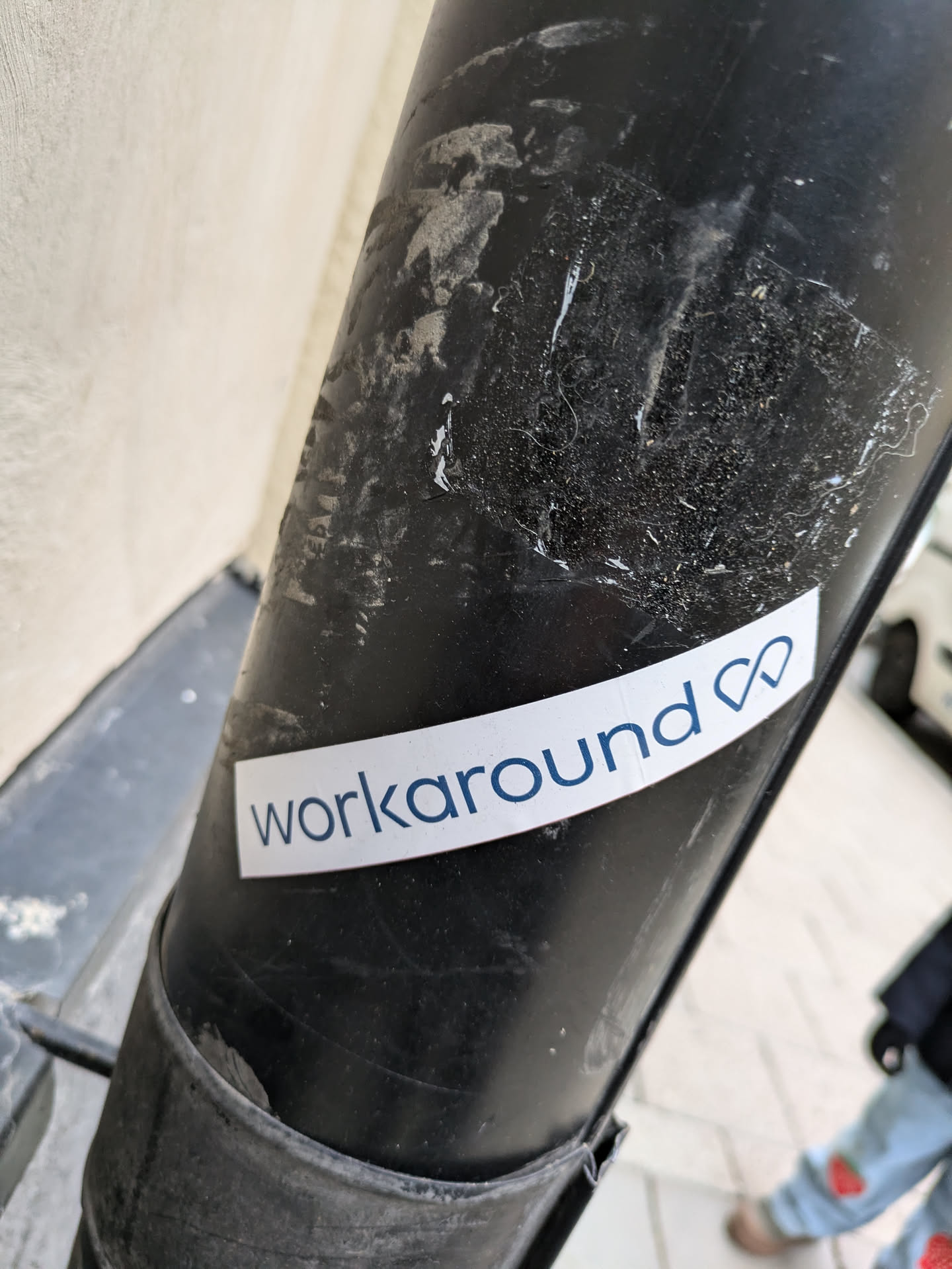 A white sticker with the word 'workaround' and an infinity symbol in blue text is affixed to a dark-colored pole.