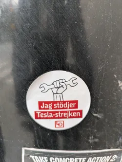A round sticker expressing support for the Tesla strike. It features an illustration of a fist holding a wrench and the text "Jag stödjer Tesla-strejken" (I support the Tesla strike) in Swedish.