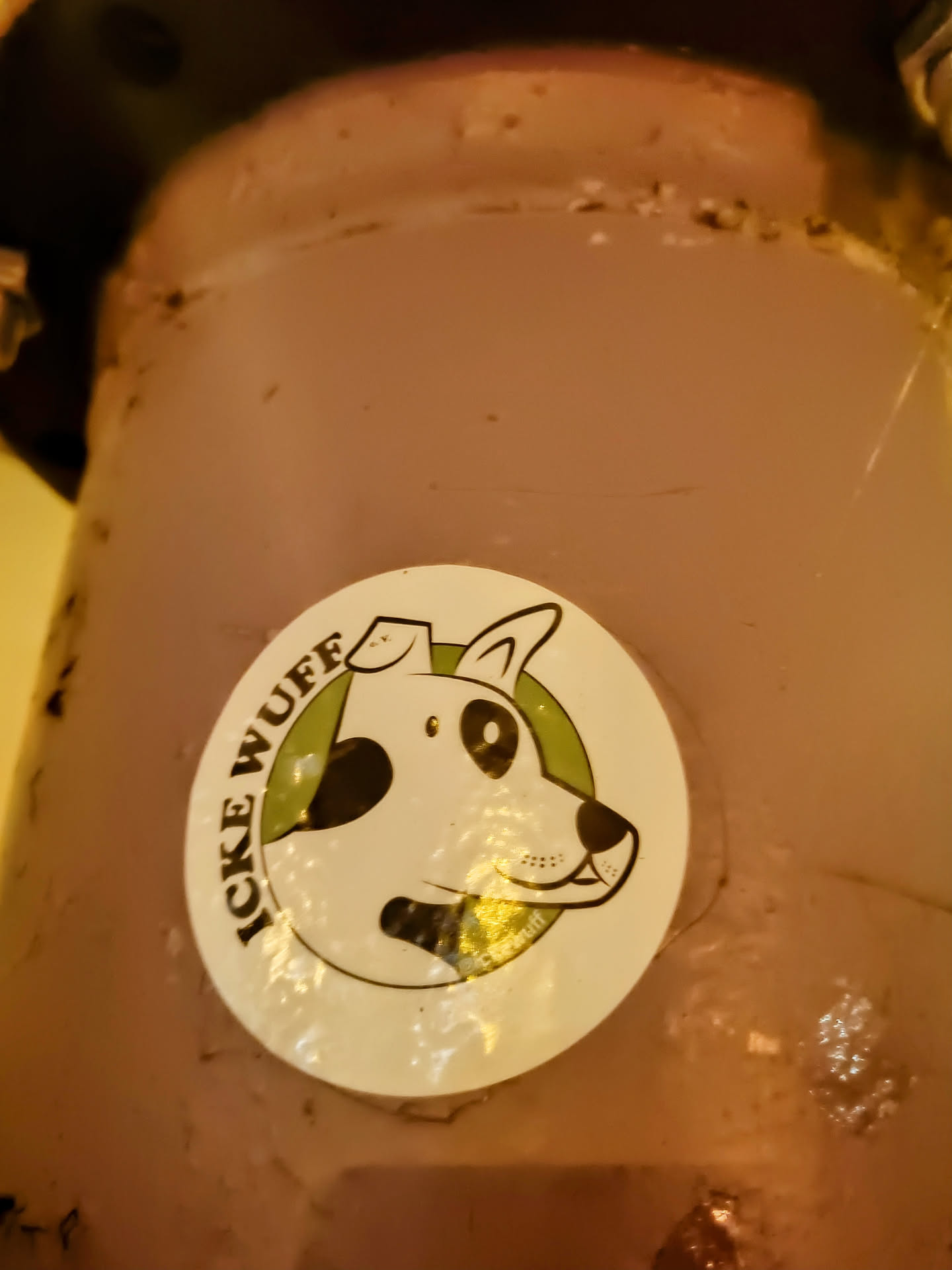 A round sticker featuring a cartoon drawing of a dog's head. The dog is white with black spots, and it has a friendly expression. The text "ICKE WUFF" is written around the dog's head, which might be a name or slogan. 