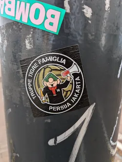 Round sticker featuring a cartoon character holding a megaphone, with text surrounding it. The text mentions 'Tigre', 'Famiglia', 'Persija', and 'Jakarta'.