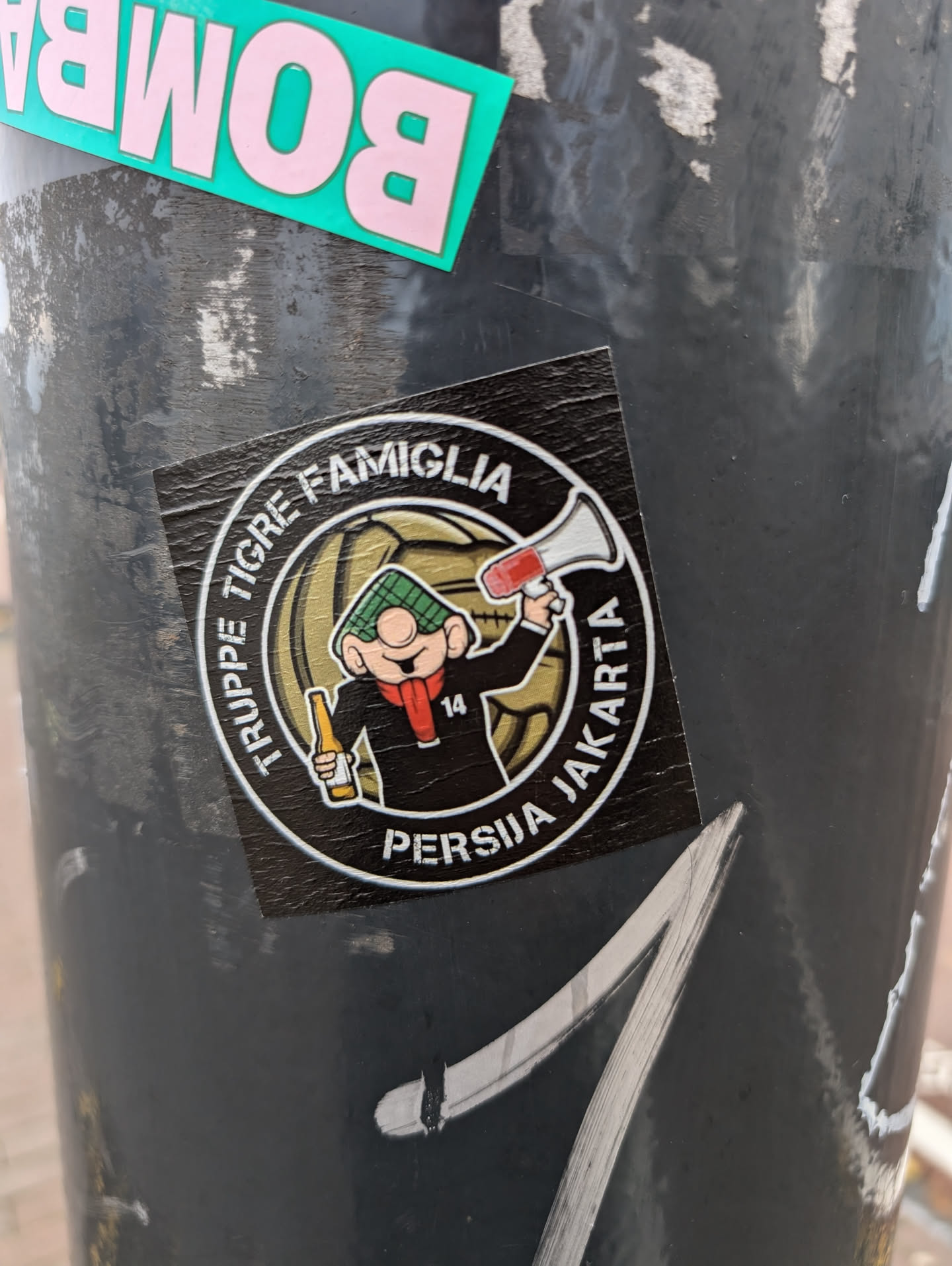 Round sticker featuring a cartoon character holding a megaphone, with text surrounding it. The text mentions 'Tigre', 'Famiglia', 'Persija', and 'Jakarta'.