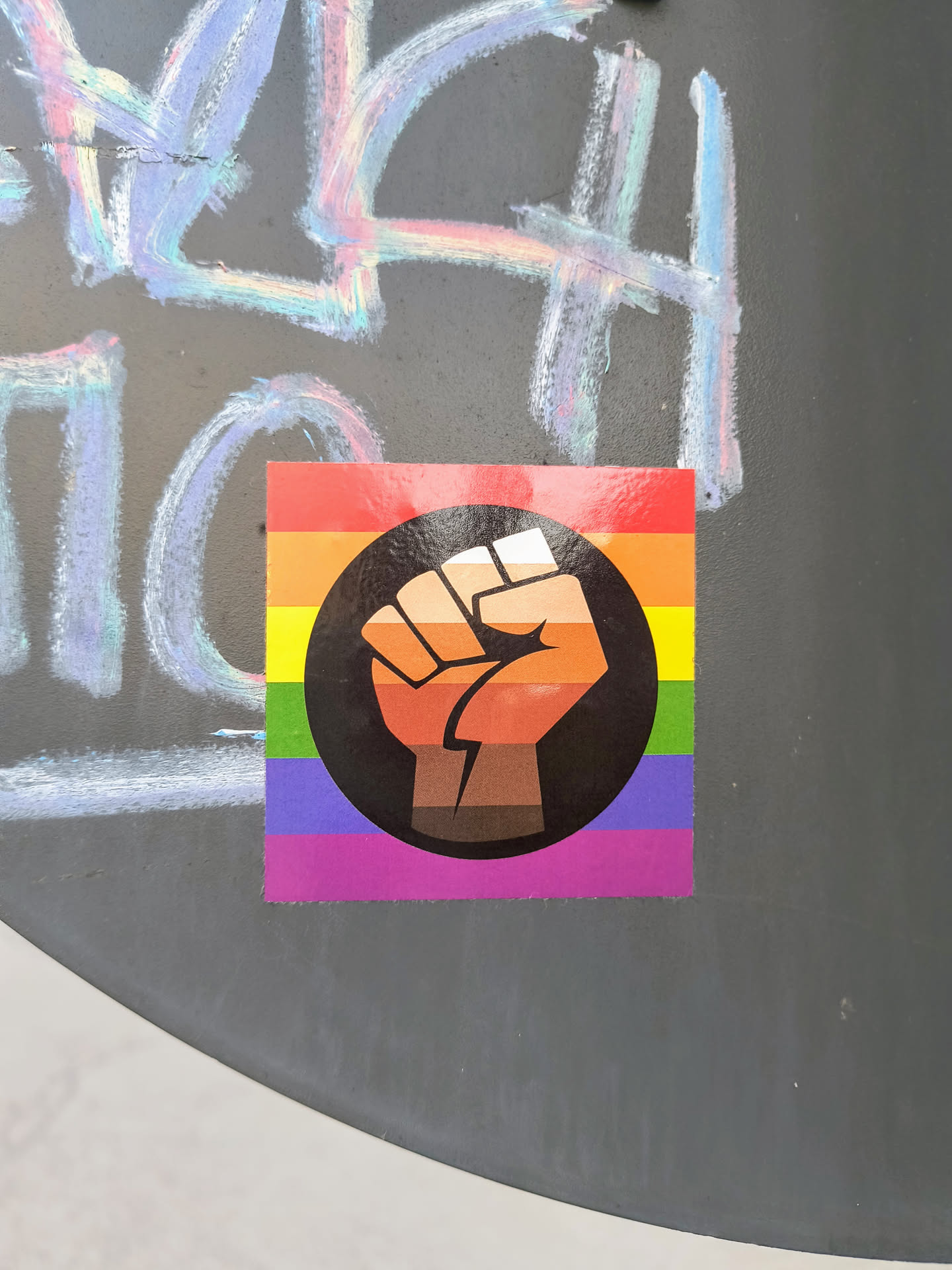 The sticker features a rainbow pride flag with a raised fist in a black circle, showcasing support for LGBT rights and racial equality. The fist is gradient and shades of brown.
