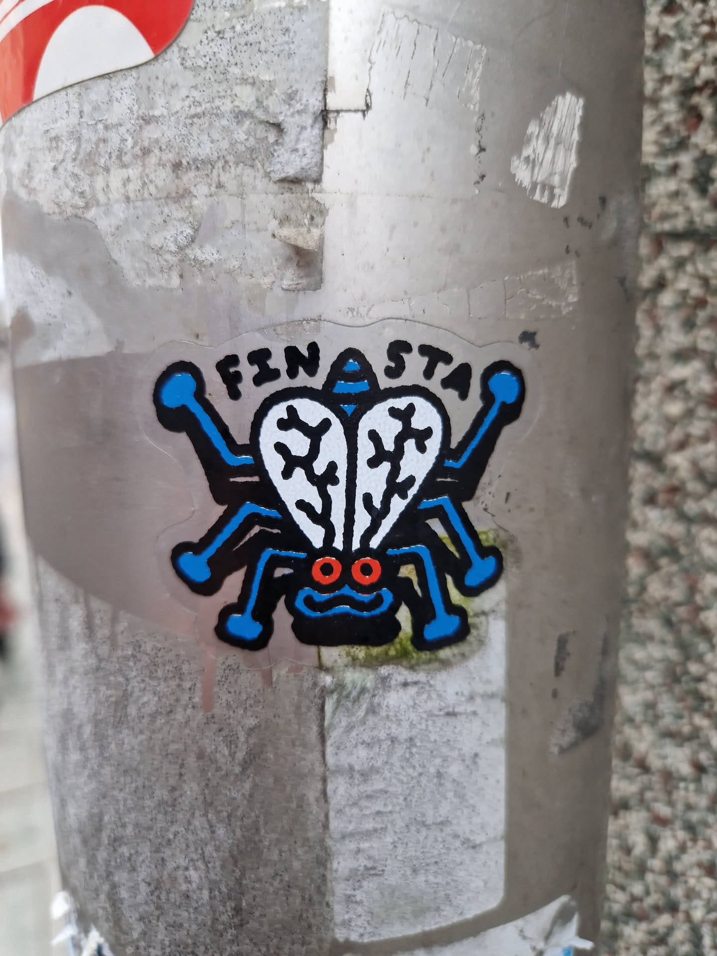 A sticker featuring a cartoon fly with blue legs and body, red eyes, and white wings. The word "FINASTA" is written above the fly.