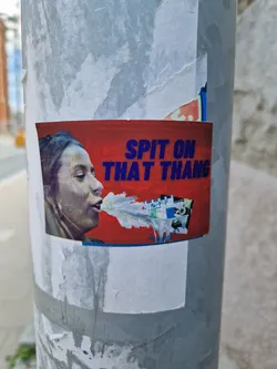 A sticker featuring a woman spitting, with the text "Spit on that thang" in bold blue letters on a red background.  The style is provocative and slightly edgy.