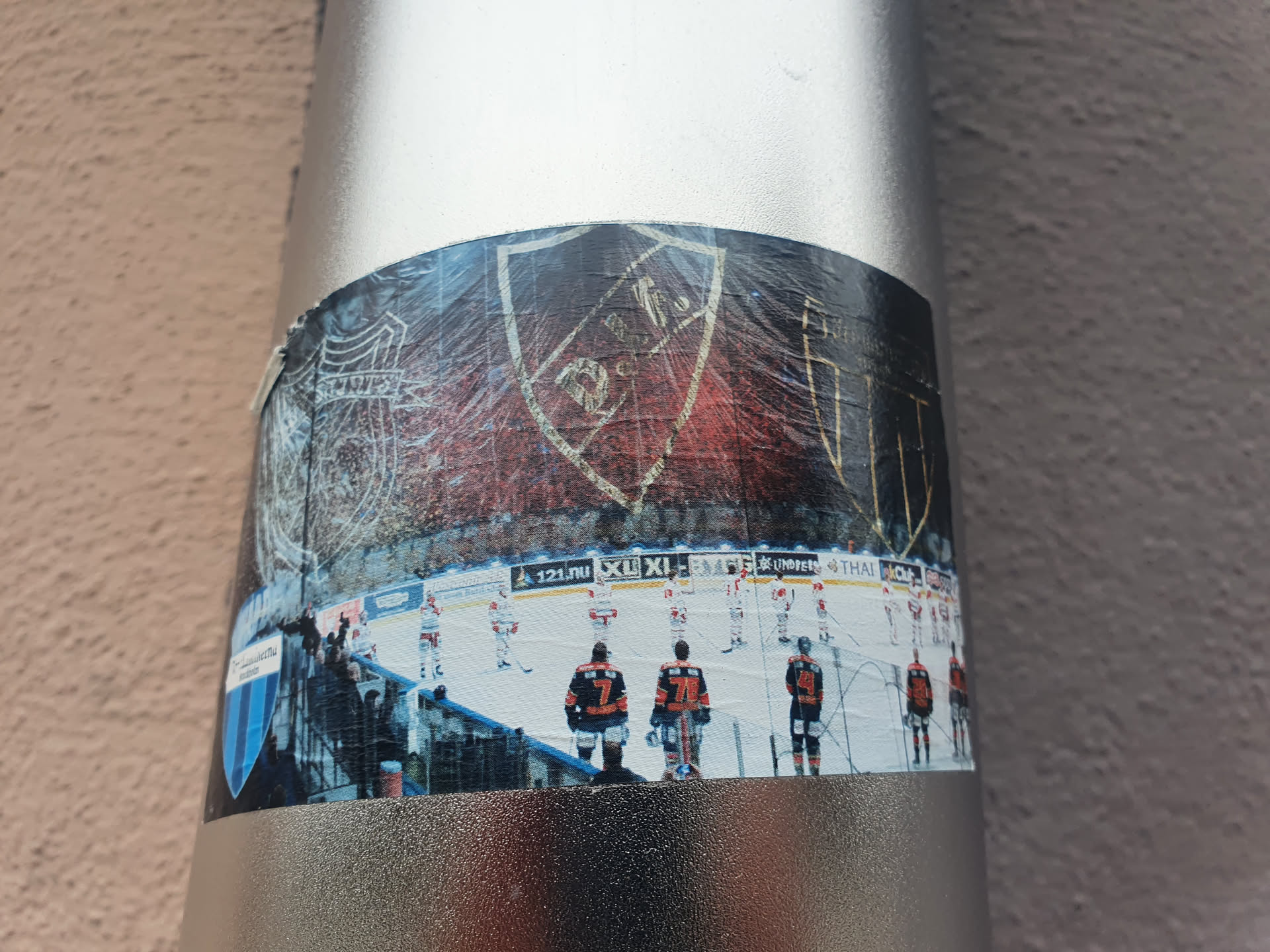 A sticker depicting an ice hockey team. The sticker includes a prominent crest, likely the team's logo, and a photo of players on the ice during a game.  The crest is a shield shape with some text that is difficult to read completely. The image quality of the sticker is slightly degraded, suggesting it may have been exposed to the elements.