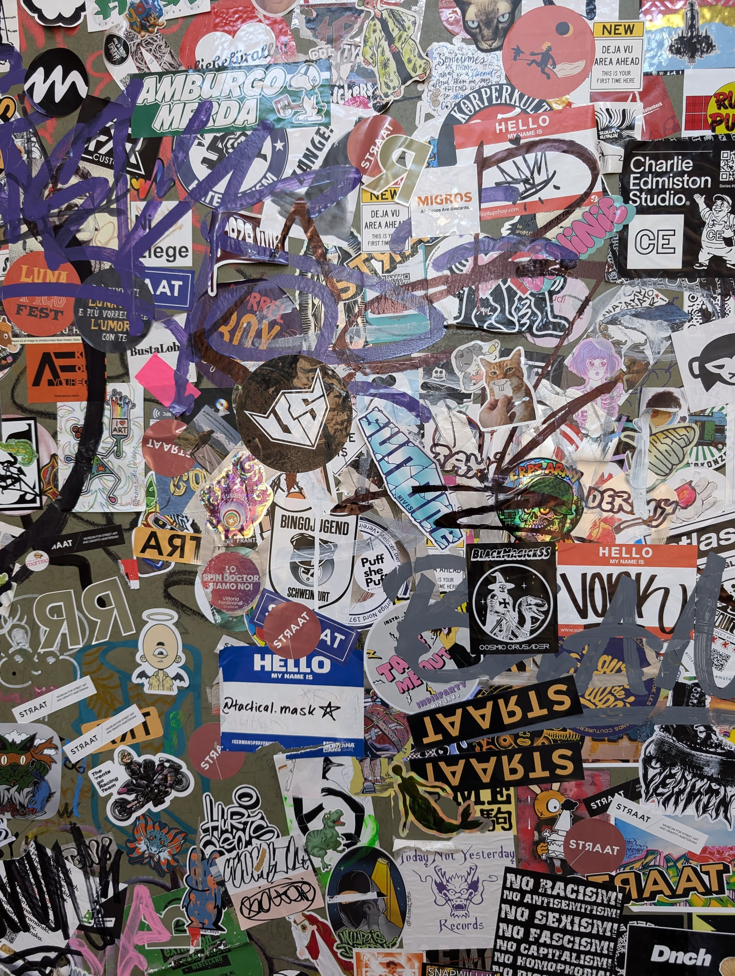 A close-up shot of a wall covered in a multitude of stickers. The central sticker displays the text "Radical mask".  Many other stickers have illegible text, while some show logos and imagery. The overall aesthetic is one of urban grit and artistic expression. 