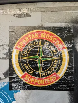 A worn sticker showing a compass with Spartak Moscow written around it. The words 'Supporters' are at the bottom.  The design incorporates elements reminiscent of Stone Island branding. The sticker shows significant wear and tear.