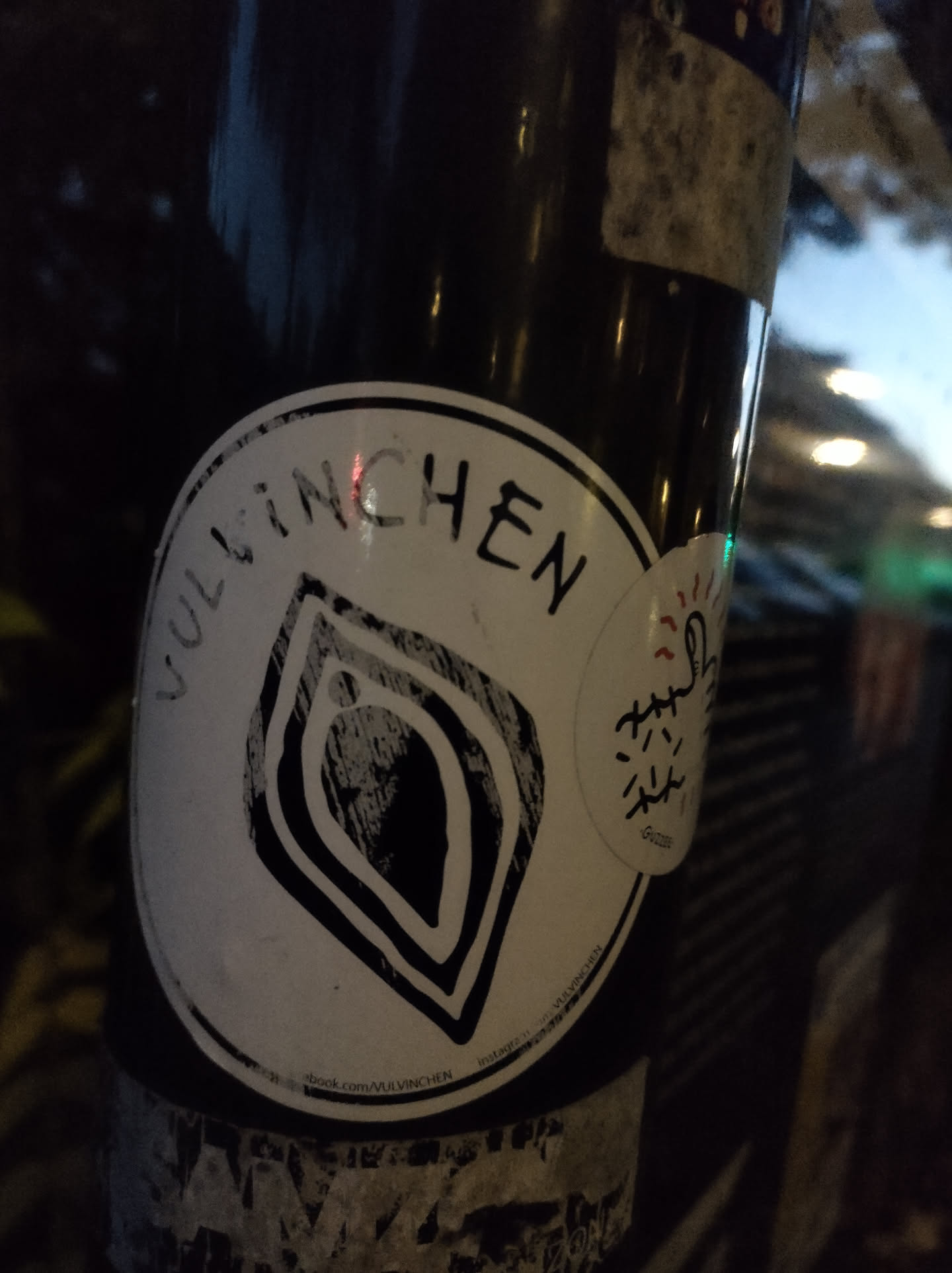 A black and white sticker with the word Vulinchen and a stylized leaf-like design.  The sticker is affixed to a dark pole.