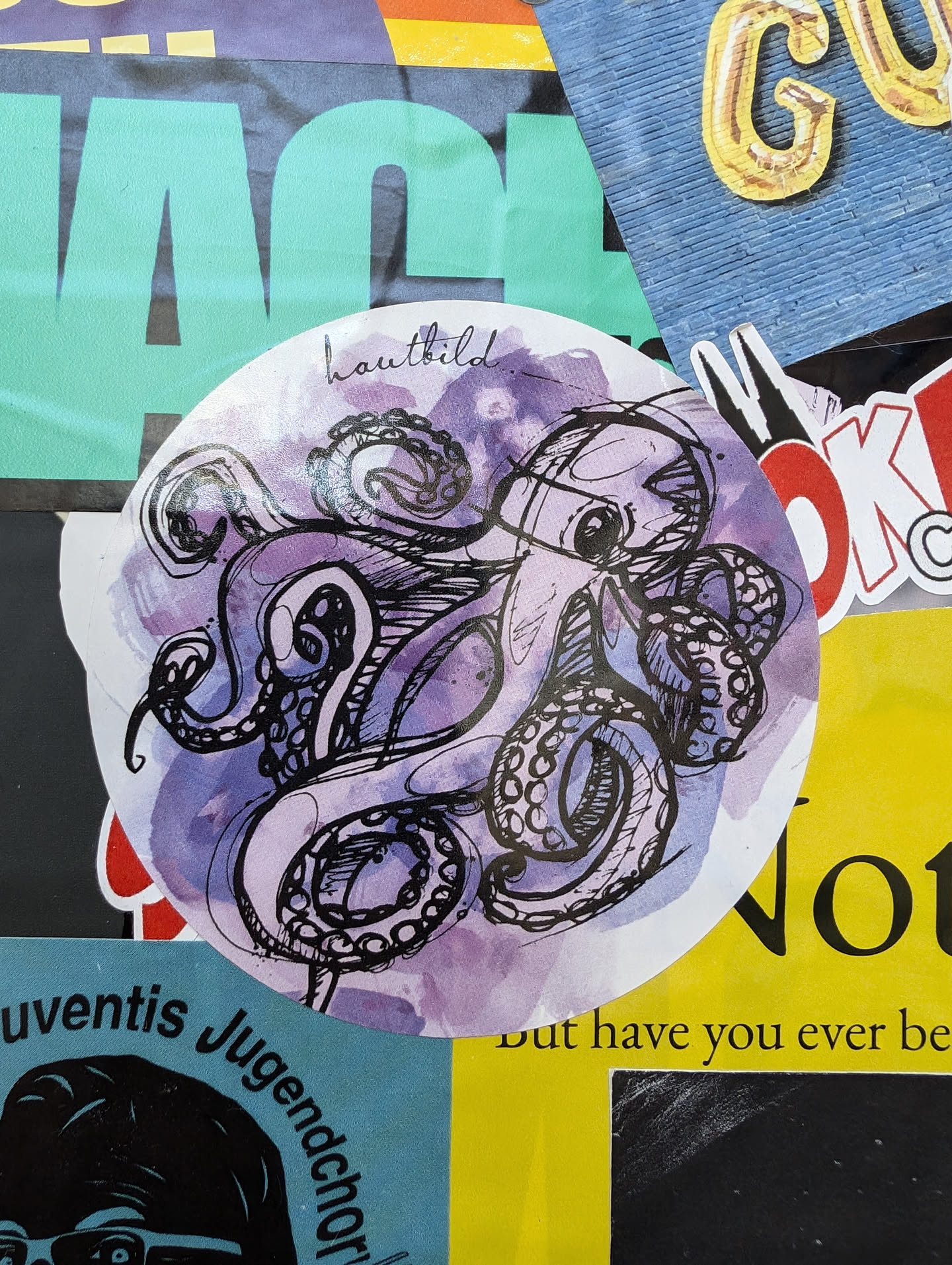 Round sticker featuring a watercolor-style illustration of an octopus. The octopus is drawn in black ink with purple watercolor washes in the background. The word "hautbild" is written in a small font at the top of the sticker.