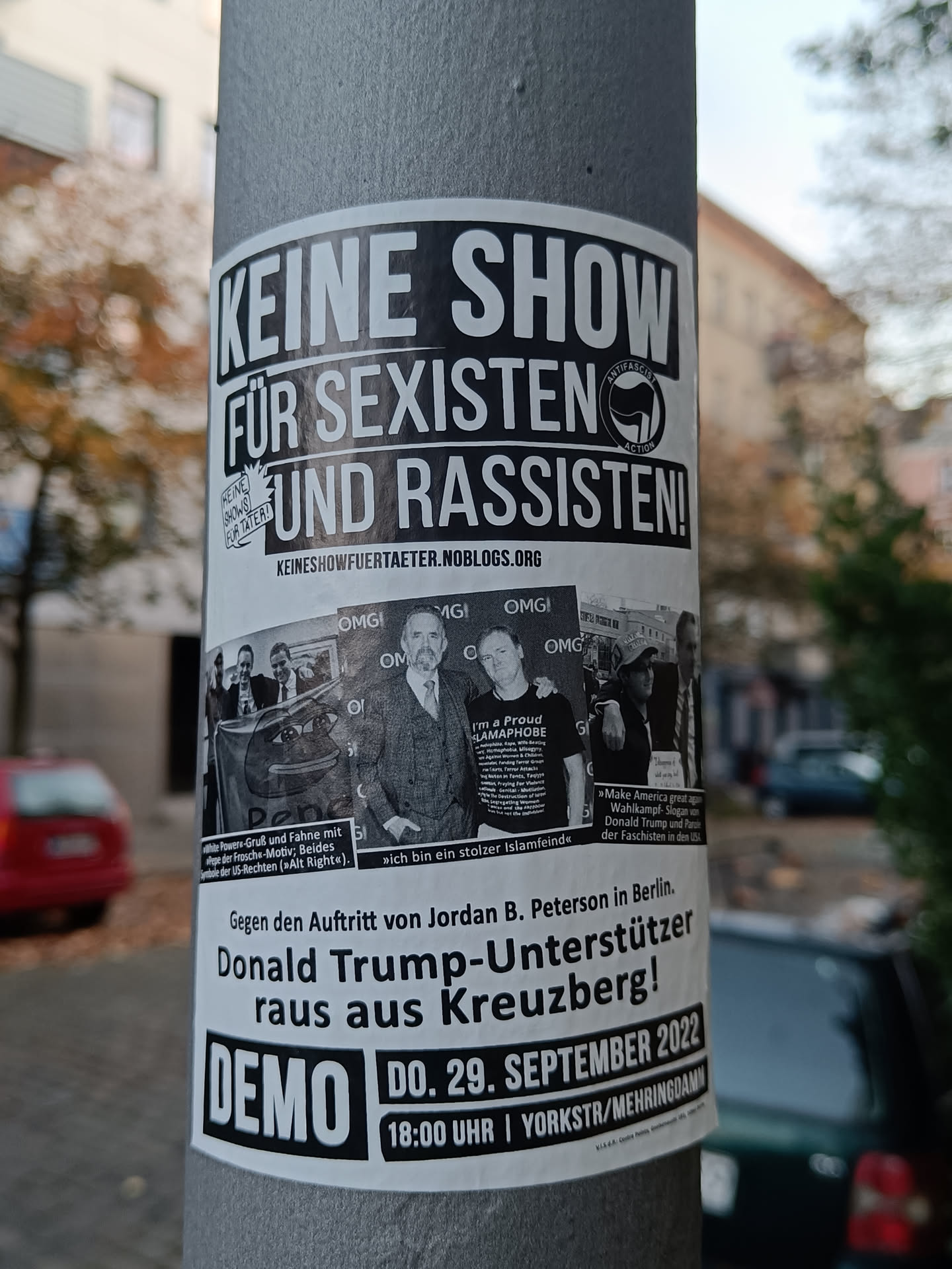 A black and white sticker on a pole protesting against Jordan B. Peterson's  show in Berlin, calling him a supporter of Donald Trump. It promotes a demo on September 29th, 2022 at 6 PM.
