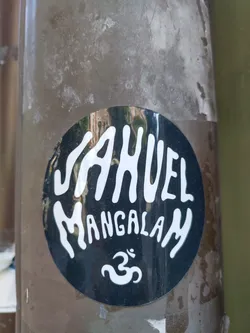 A round black and white sticker with the text JAHUEL MANGALAM and the Om symbol. The sticker is attached to a brown pole.