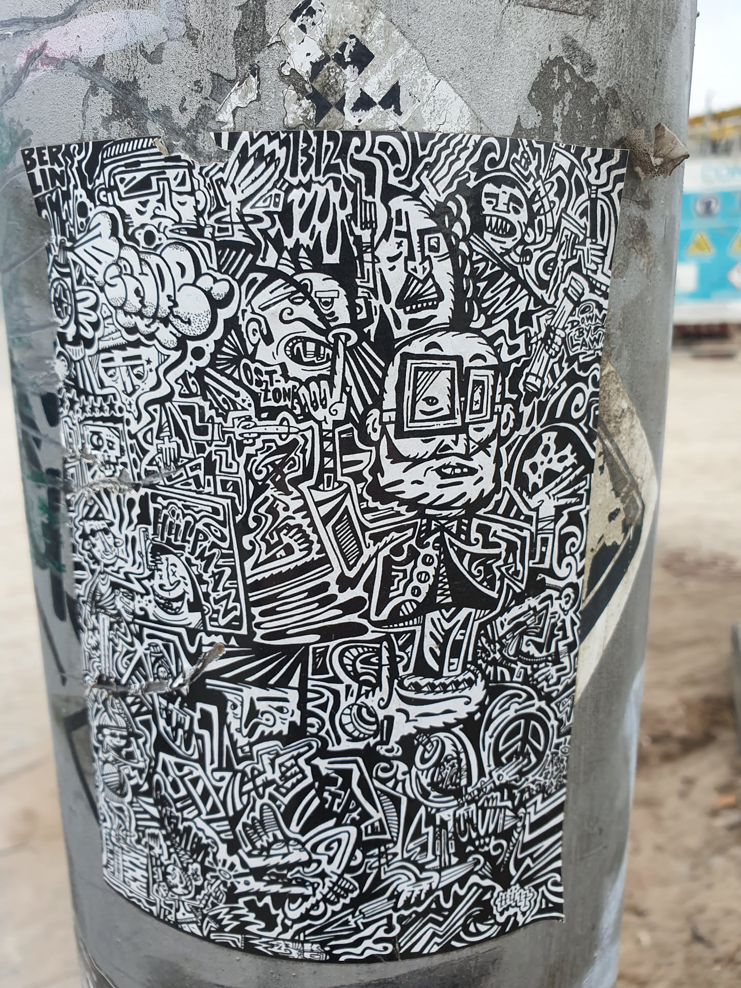A sticker with a dense composition of black and white doodles. It features various abstract shapes, faces, and symbols, creating a chaotic yet visually engaging pattern. The style is reminiscent of graffiti or street art.