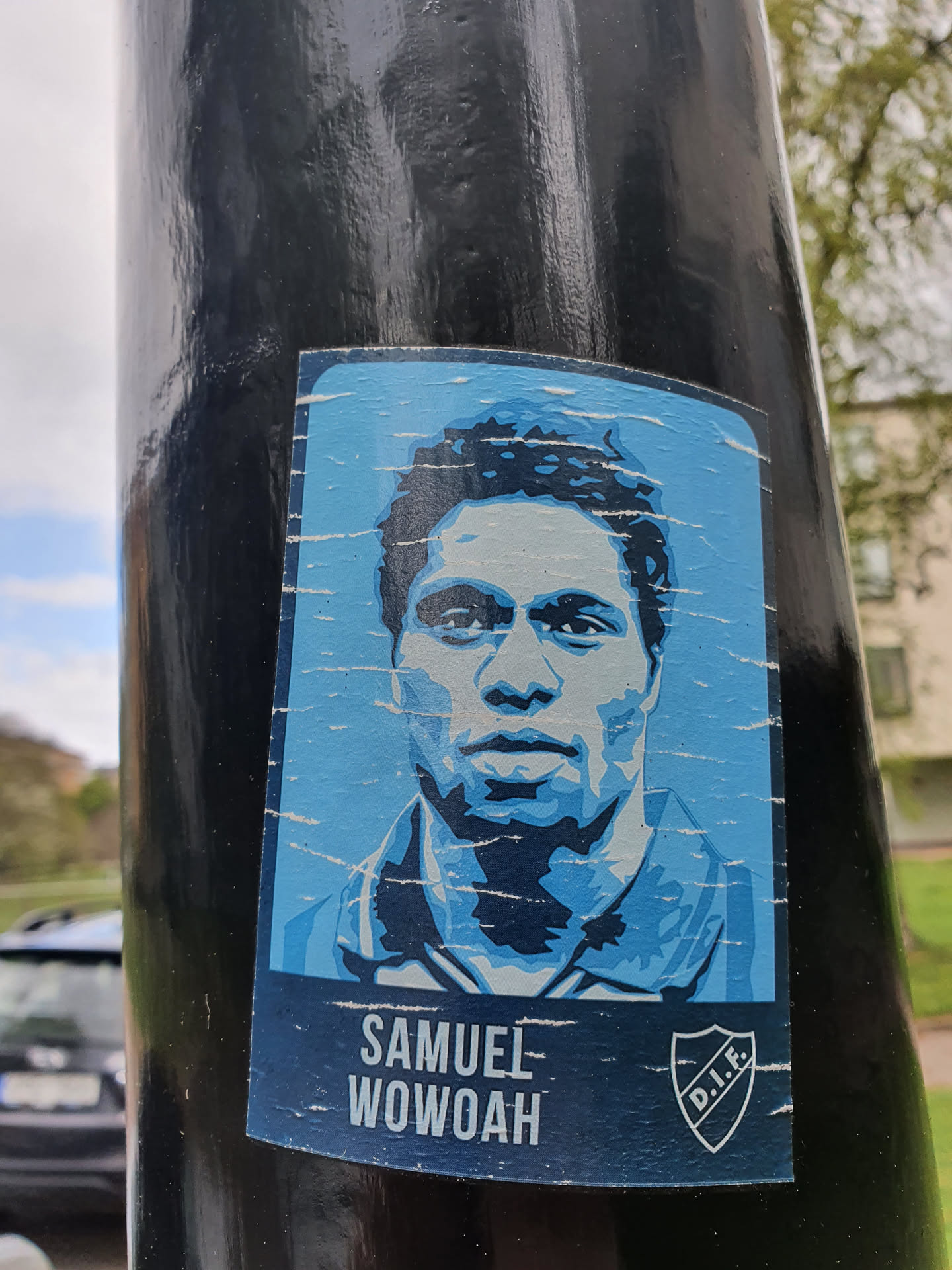 A sticker featuring a stylized portrait of Samuel Wowoah, a player likely associated with the D.I.F. (presumably a football club). The sticker has a worn, slightly distressed look, suggesting it may have been placed outdoors for some time. 