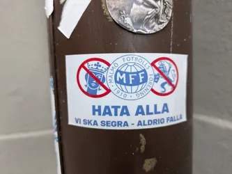 A sticker expressing loyalty to Malmö Fotbollsförening (MFF).  It features a prohibition symbol over the coat of arms of Sweden and another emblem, with the text "Hata Alla" (Hate All) and "Vi ska segara - Aldrig falla" (We shall conquer - Never fall).