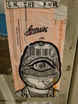 Black and white sticker art depicting a face with a barcode on its forehead and a large eye. The sticker is on top of an old postage label.