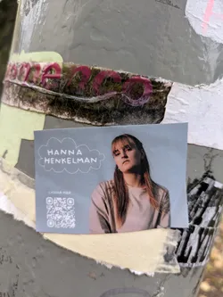 A sticker featuring a portrait of Hanna Henkelman, a musician, with a QR code linking to her music. The sticker has a light blue background and features a minimalist design.