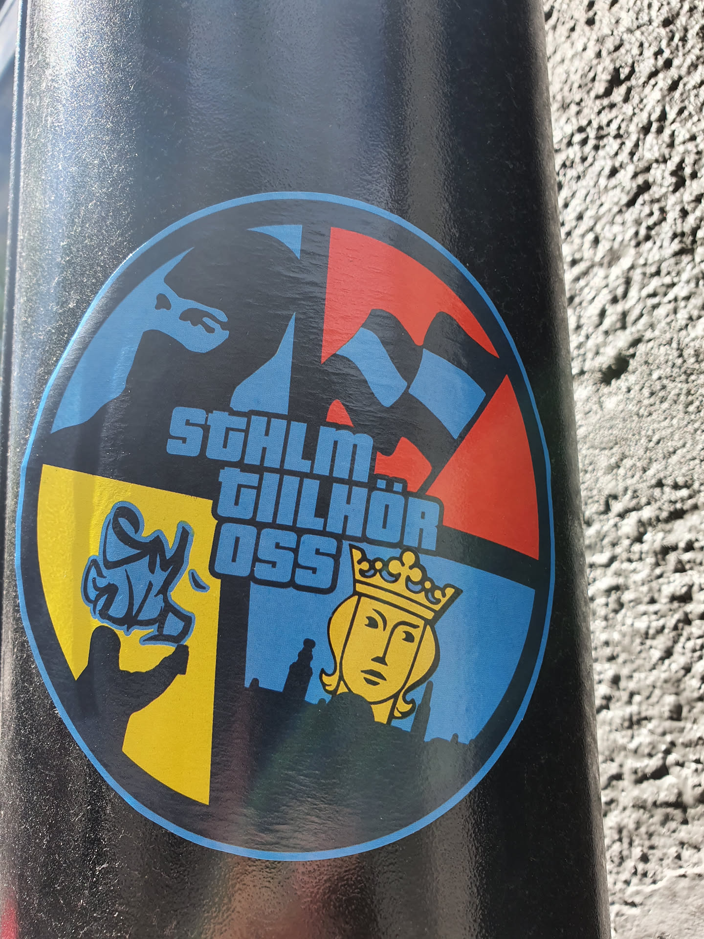Round sticker with a design divided into four sections: a blue section with a stylized flag, a red section with a wavy flag, a yellow section depicting a hand with spray paint, and a blue section with a crowned figure resembling a queen over a cityscape. The text "STHLM TILLHÖR OSS" is prominently displayed.
