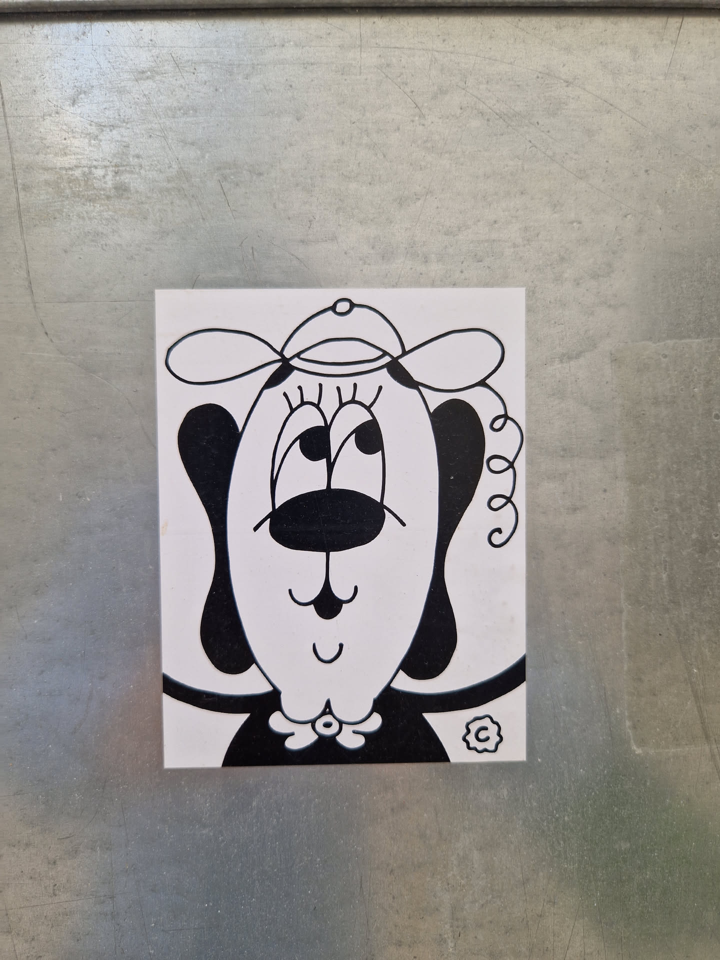 This sticker features a charming illustration of a dog with a simplistic design. The dog is depicted wearing a hat, and its facial expression is friendly and approachable. The overall style is minimalistic yet expressive.