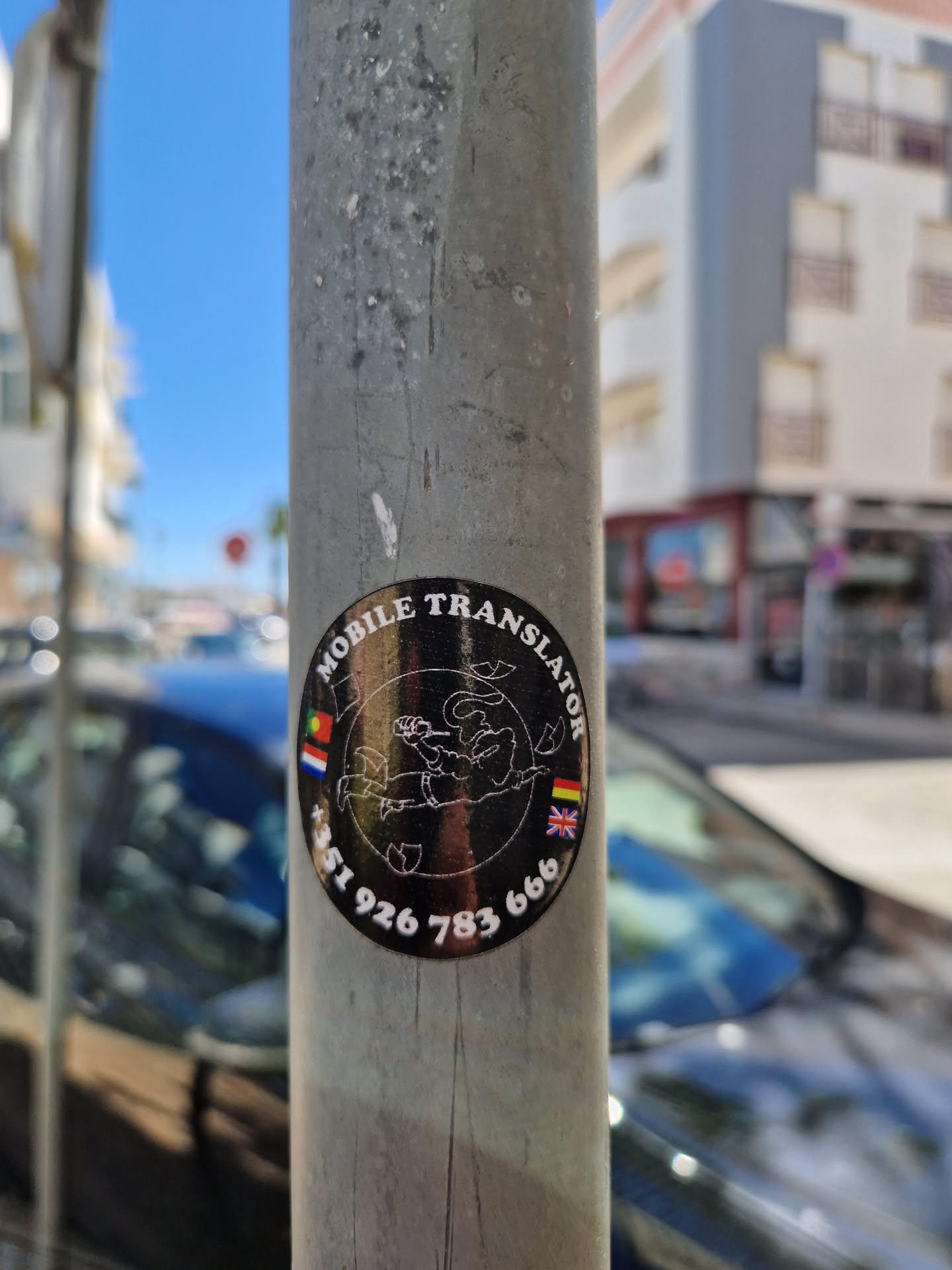 A round, black and gold sticker advertising mobile translation services. It features a stylized graphic of a person possibly representing translation and includes the phone number +351 926 783 666 and flags representing several countries.