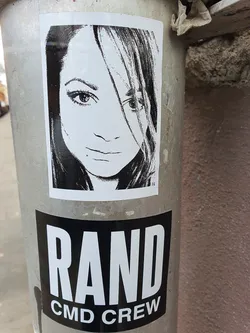 A black and white sticker featuring a portrait of a woman.  Below the portrait is a second sticker with the text "RAND CMD CREW".