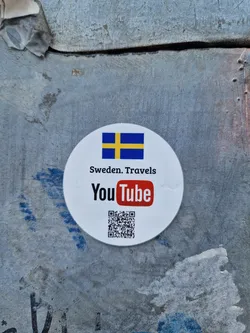 Round white sticker with the flag of Sweden, the YouTube logo, and a QR code.  The text 'Sweden. Travels' is also present.