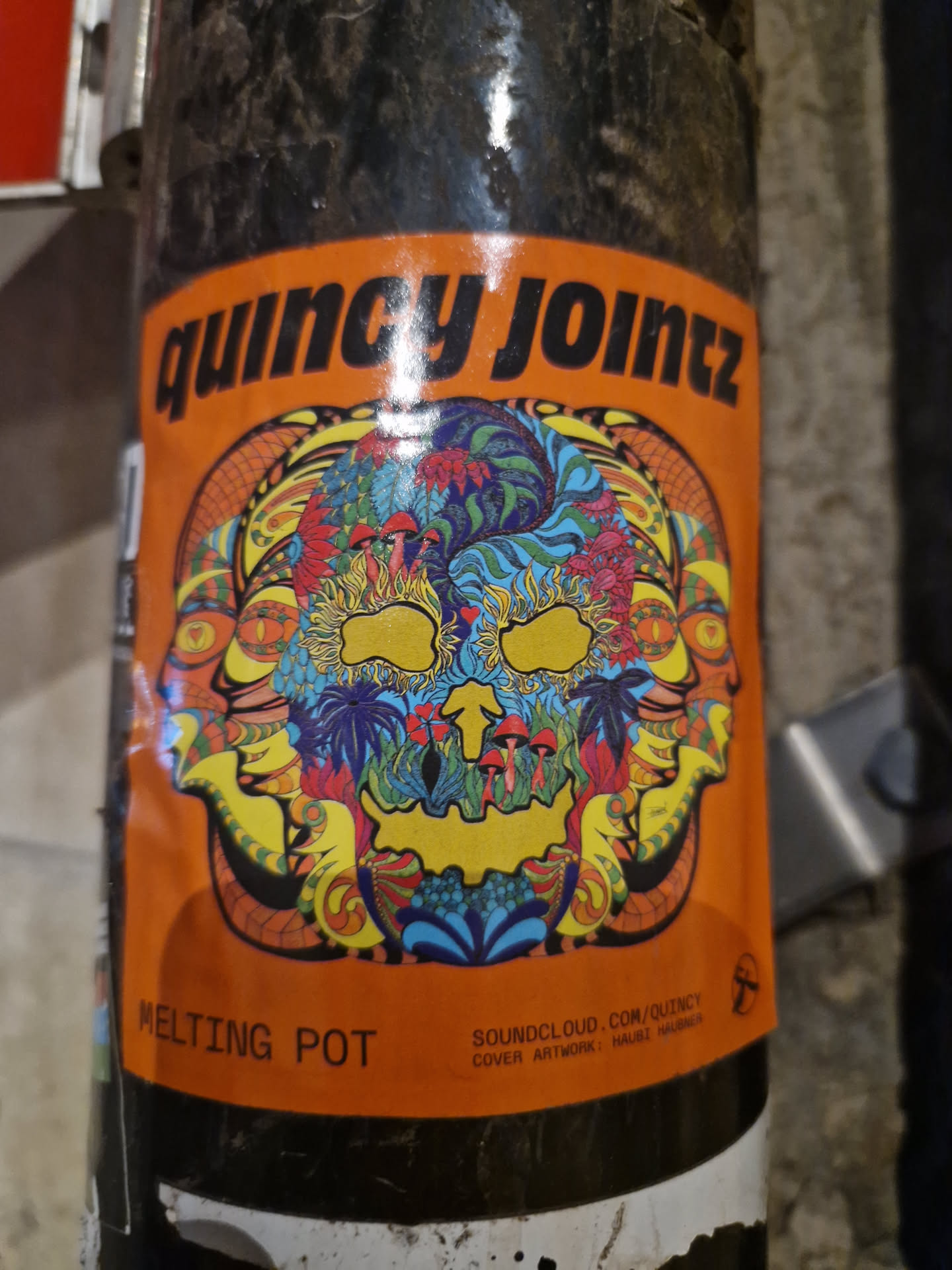 Psychedelic skull sticker with vibrant colors and intricate details. The sticker features a melting pot design with multiple faces surrounding a central skull, all adorned with floral and mushroom motifs.  Text on the sticker includes "Quincy Jointz", "Melting Pot", and a SoundCloud link.